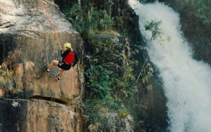 Femme qui escalade une falaise à côté d'une chute d'eau.